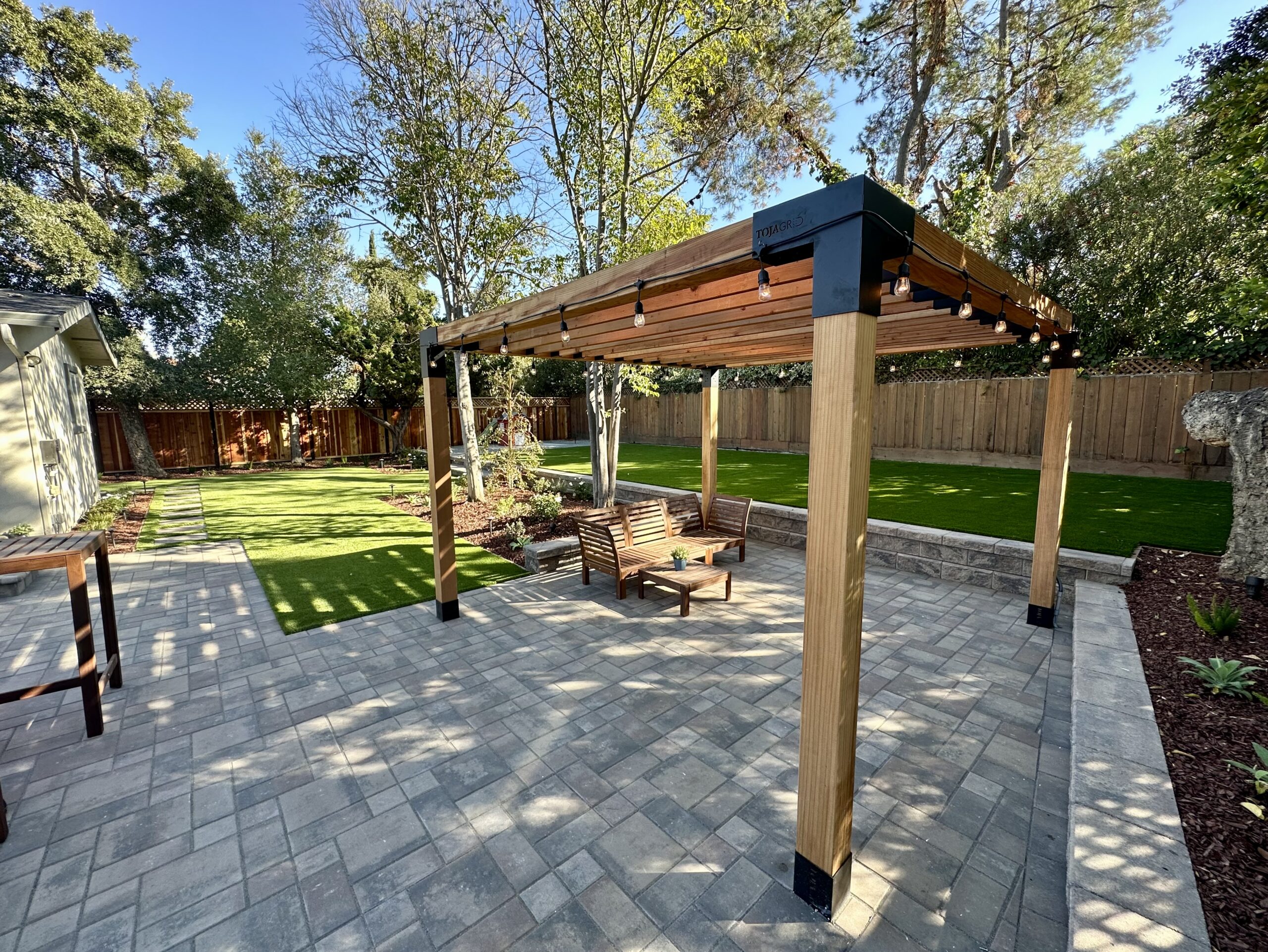 Paver patio with a wood pergola and green lawn in a backyard