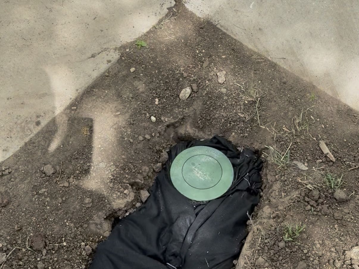 Green pop-up drainage emitter set at the end of a fabric-lined drain trench