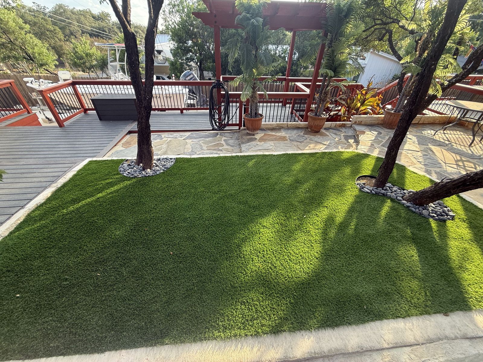 Artificial turf yard next to a flagstone patio and red pergola